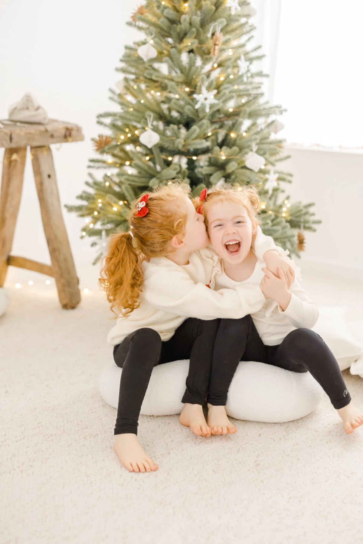 Deux petites filles riant aux éclats devant un sapin de Noël illuminé lors d'une séance photo en studio
