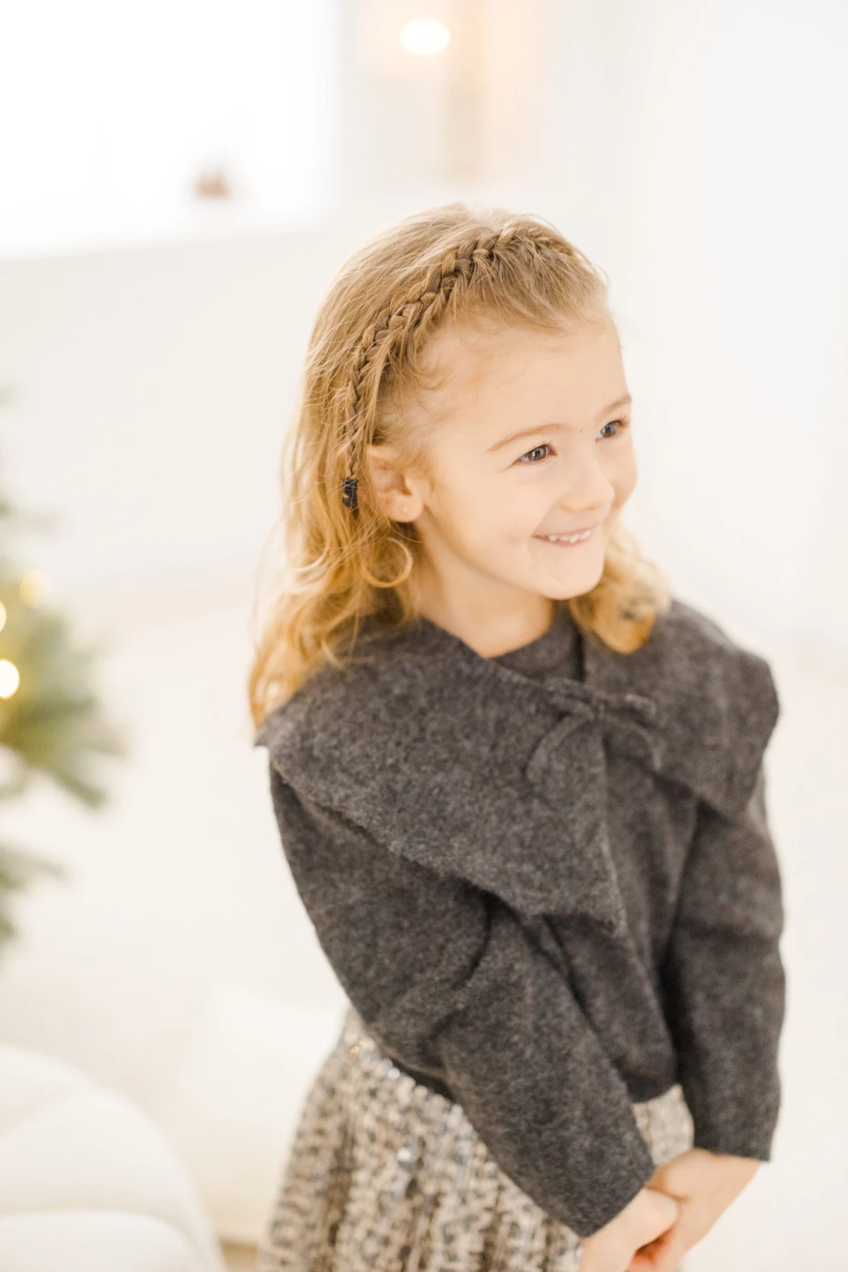 Portrait d'une petite fille blonde souriante en pull gris et jupe pailletée dans une ambiance de Noël