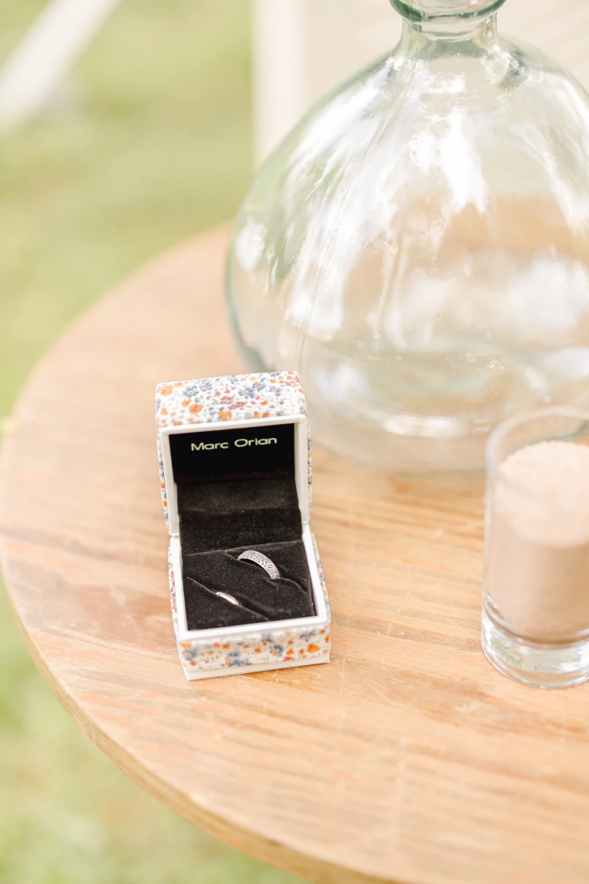 Écrin d'alliance posé sur une table en bois naturel avec décoration florale minimaliste