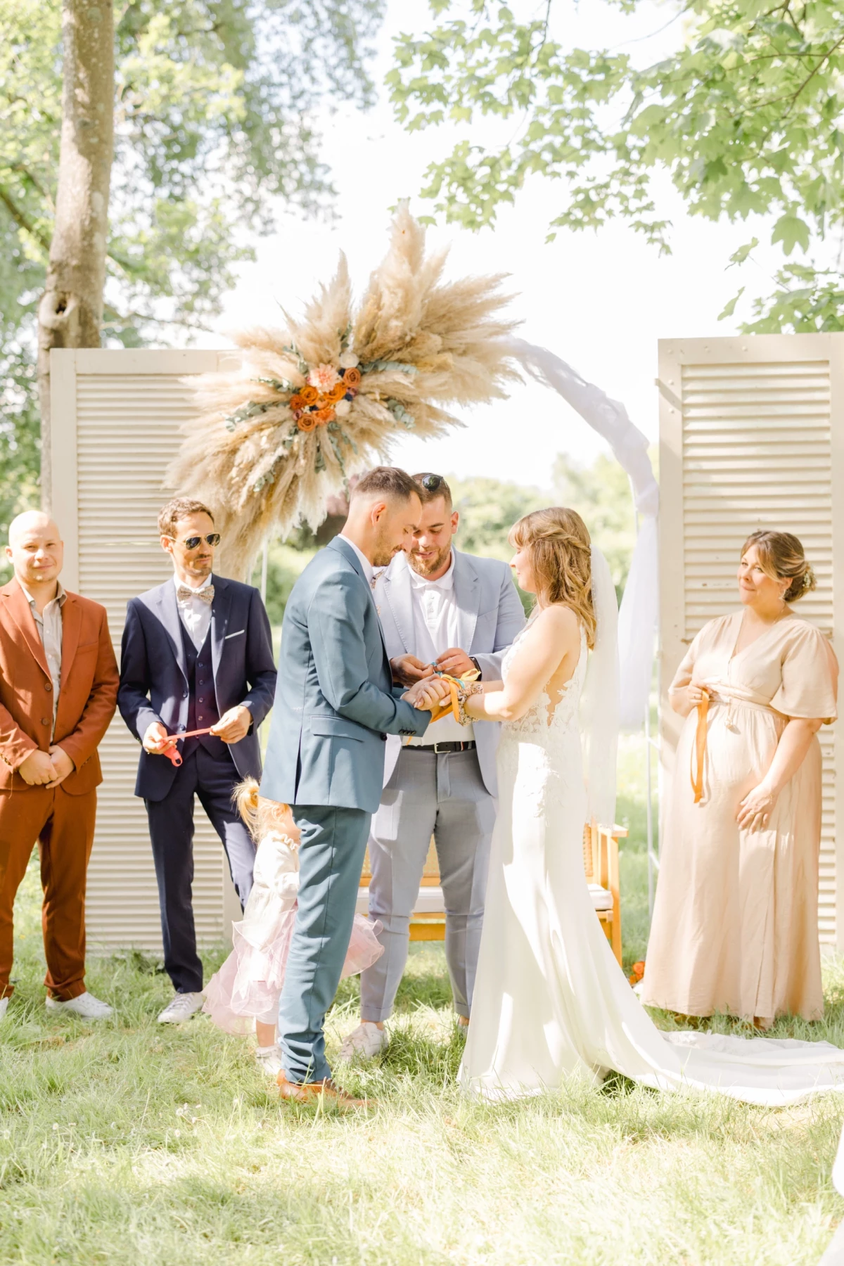 Couple de mariés s'échangeant leurs vœux sous une arche fleurie de pampas lors d'une cérémonie laïque