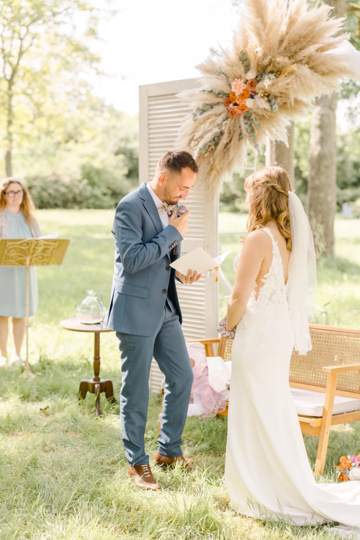 Couple de mariés échangeant leurs vœux lors d'une cérémonie laïque en plein air sous un arc floral bohème