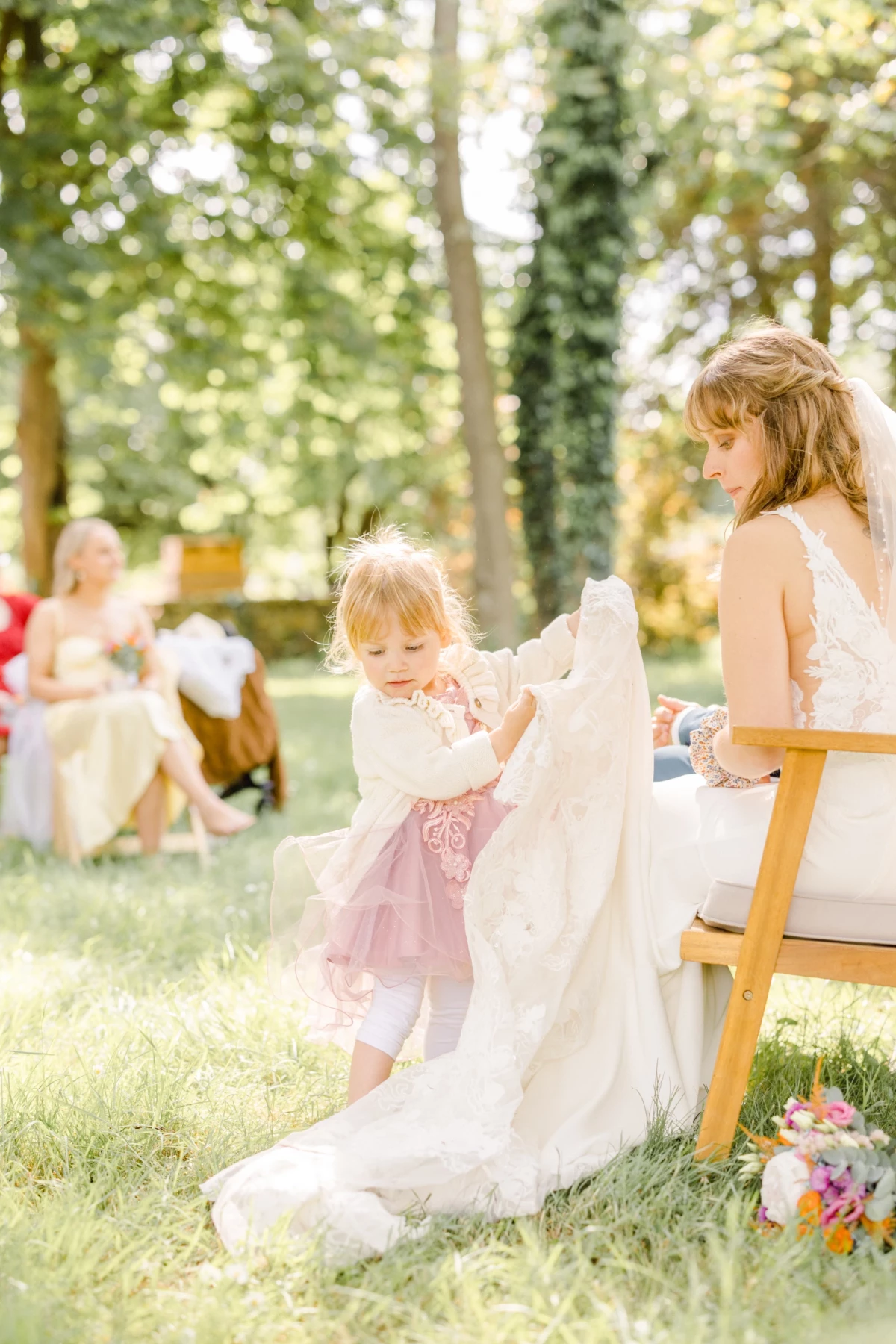 Petite fille en tutu rose jouant avec la traîne de la robe de mariée lors d'une cérémonie en plein air