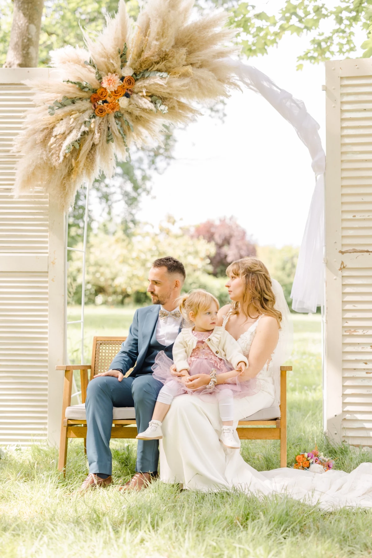 Famille réunie lors d'un mariage sous un arc fleuri de pampas, parents et enfants assis sur un banc vintage