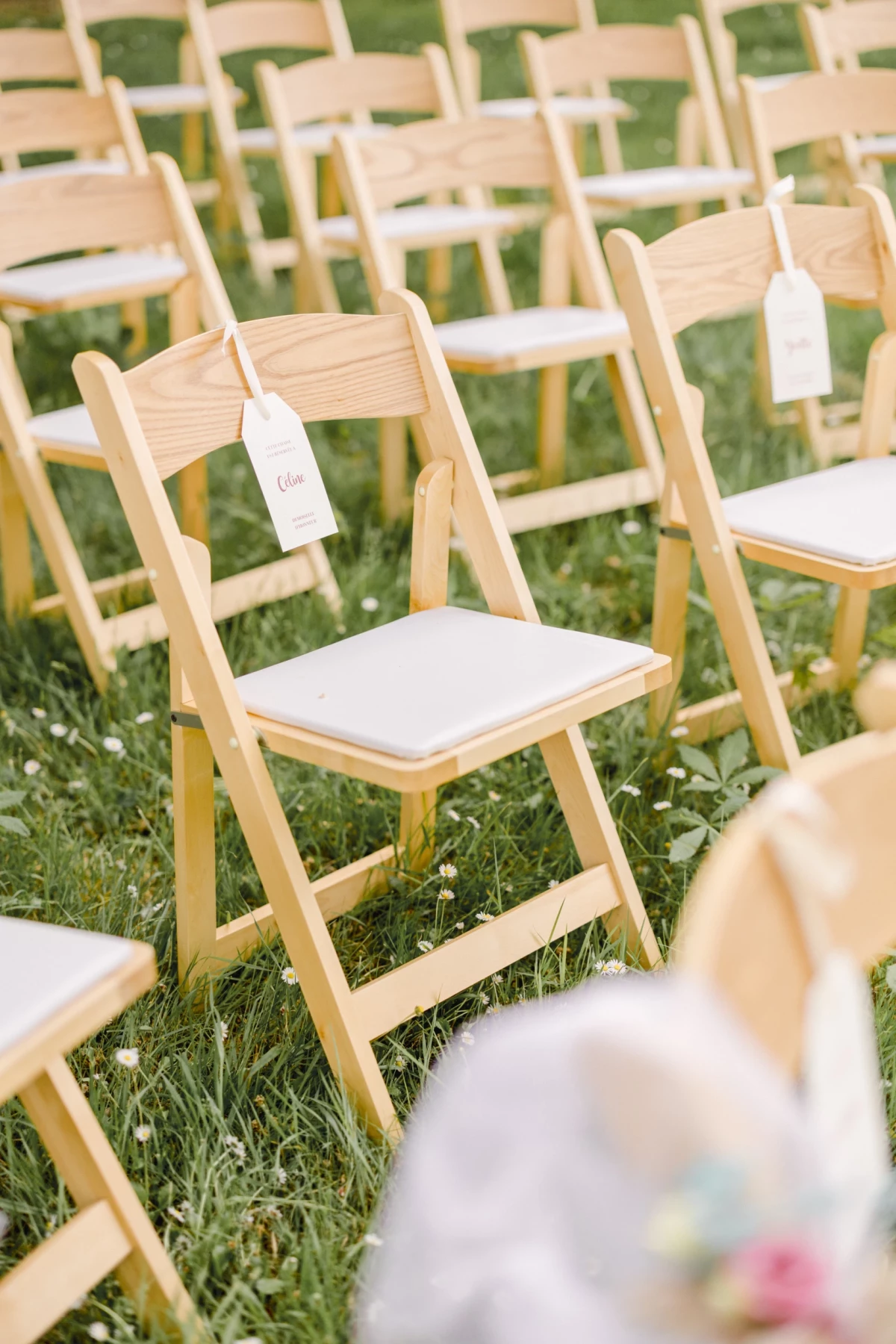 Rangées de chaises en bois blond aux assises blanches disposées sur l'herbe pour une cérémonie de mariage