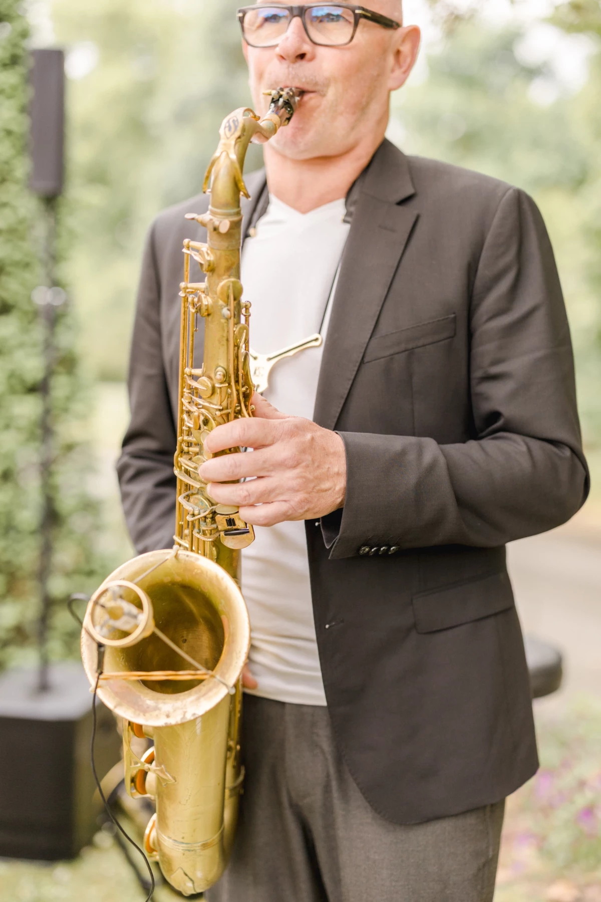 Musicien jouant du saxophone doré lors d'un mariage en extérieur, costume gris élégant