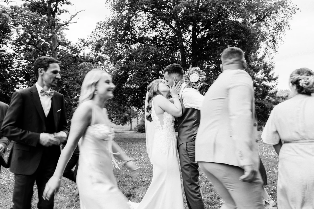 Mariés s'embrassant pendant la cérémonie laïque en extérieur entourés de leurs invités souriants