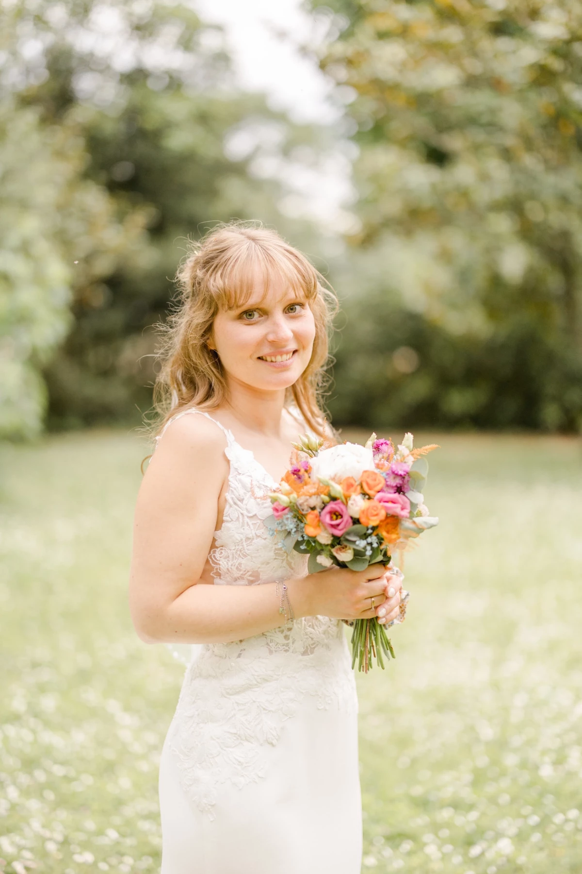 Mariée souriante tenant un bouquet coloré dans un parc verdoyant sous une lumière naturelle douce