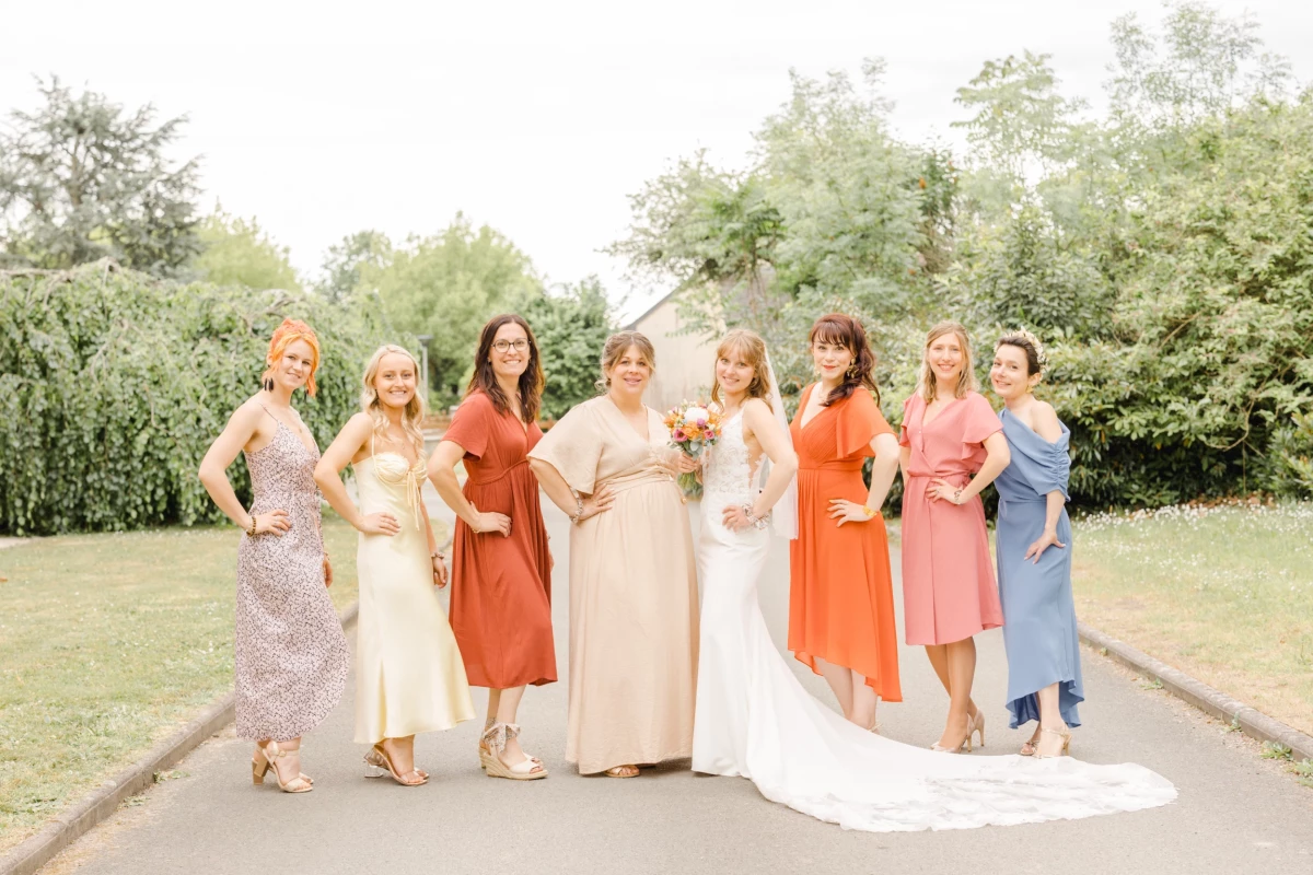 Mariée entourée de ses demoiselles d'honneur en robes colorées orange, rose et beige dans un jardin ensoleillé