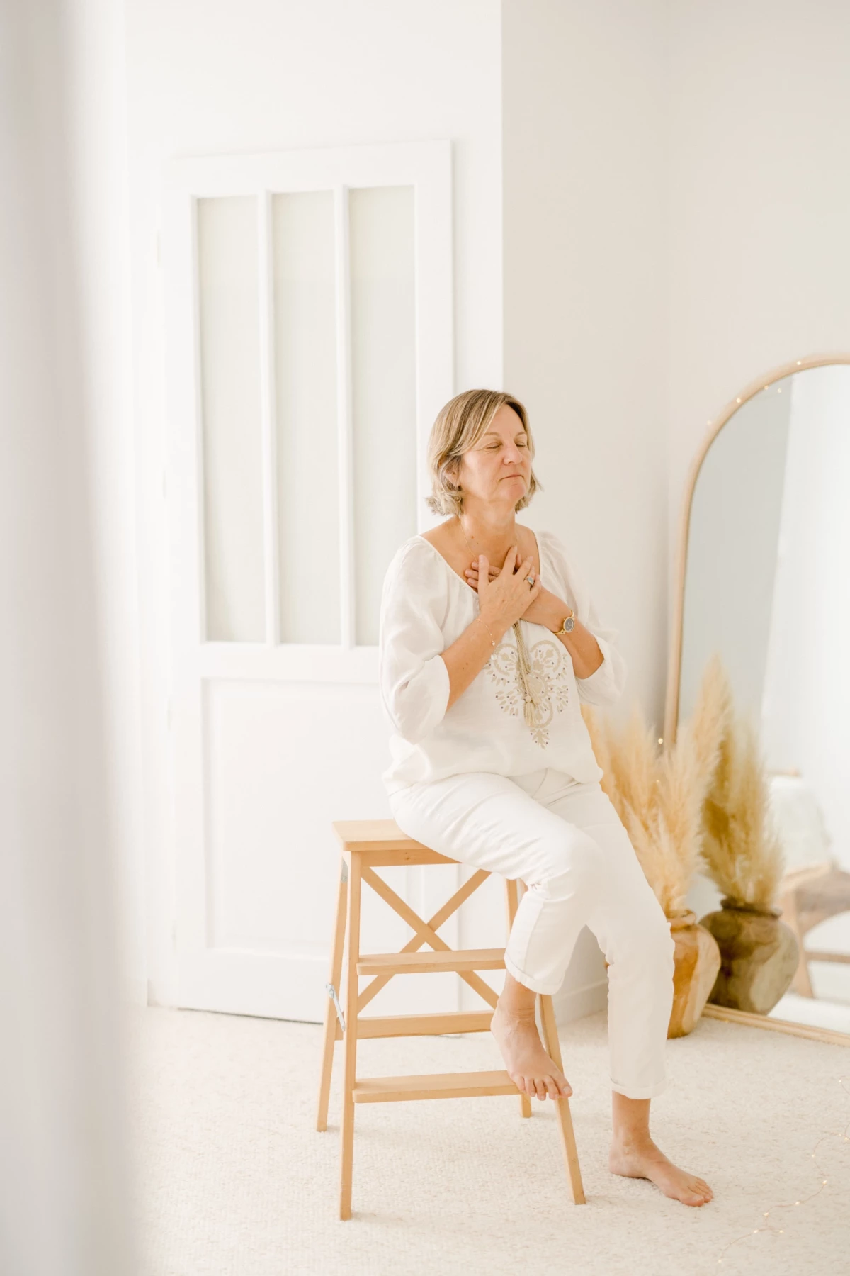 Portrait professionnel d'une femme en tenue blanche assise sur chaise en bois, mains jointes en posture méditative