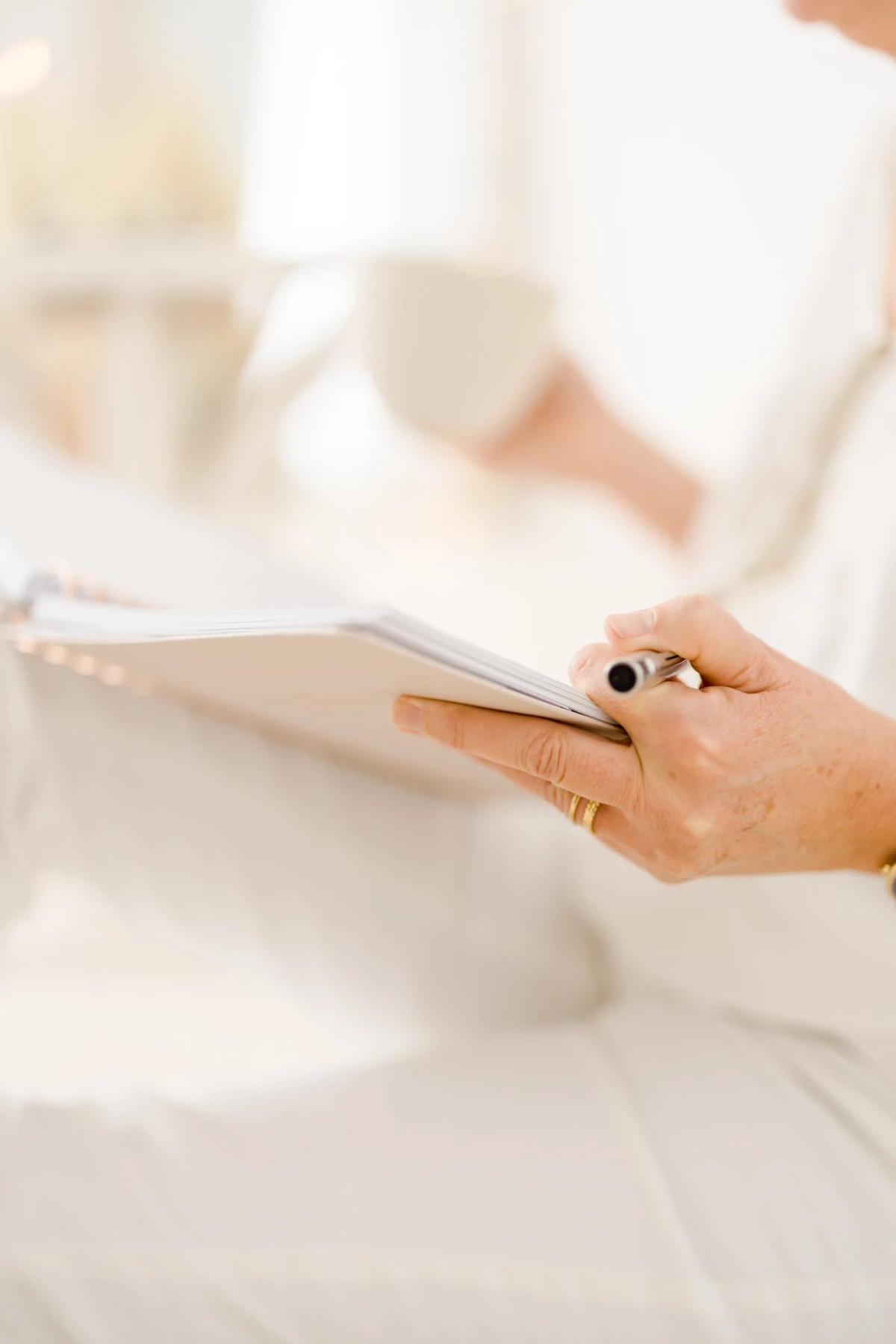 Future maman en robe blanche tenant délicatement une tablette, caressant son ventre rond dans une lumière douce