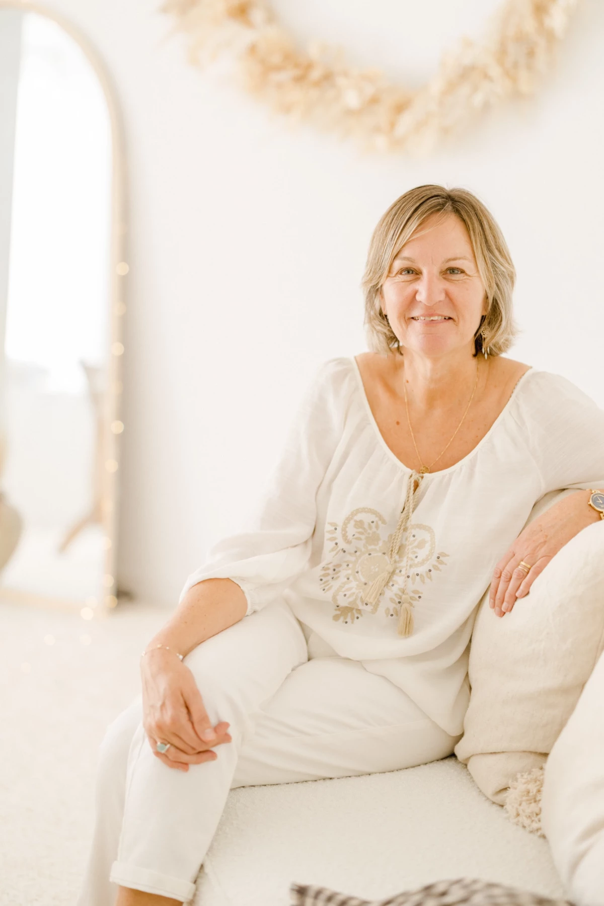 Portrait professionnel d'une femme en tenue blanche assise sur un canapé clair dans un intérieur lumineux